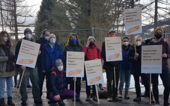 Demonstrant*innen mit Schildern vor einem Zaun von der Kampagne #fairlassen
