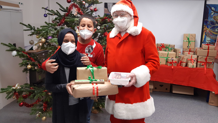 Weihnachtsmann mit Bewohner*innen und Geschenken vor dem Weihnachtsbaum